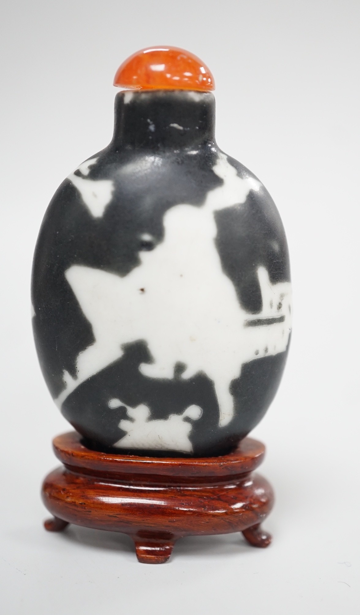 A Chinese porcelain white on black ground silhouette snuff bottle, 5.6 cm excluding stopper and wood stand